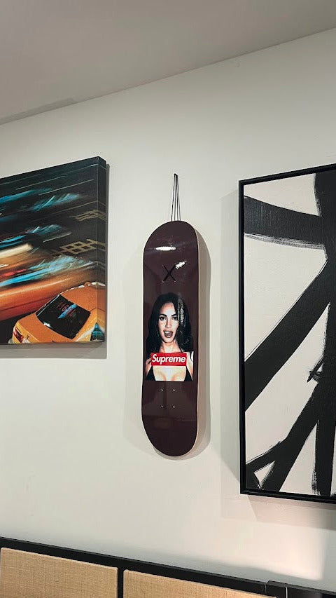 Skateboard with a printed design hanging on a wall next to other artworks.